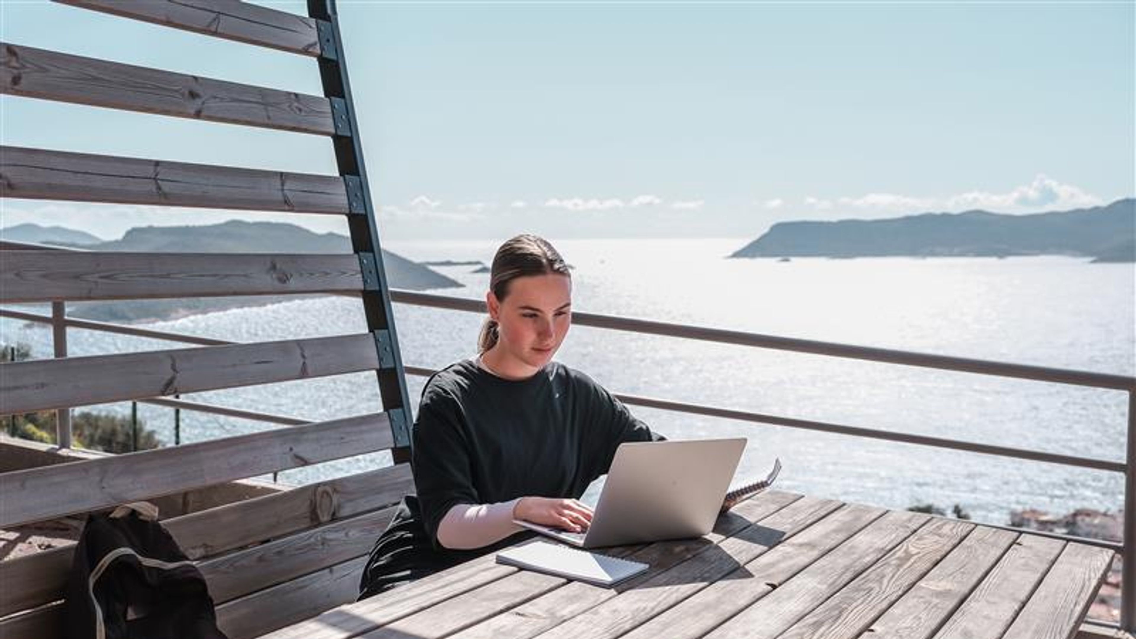 A woman working with a beach view behind 