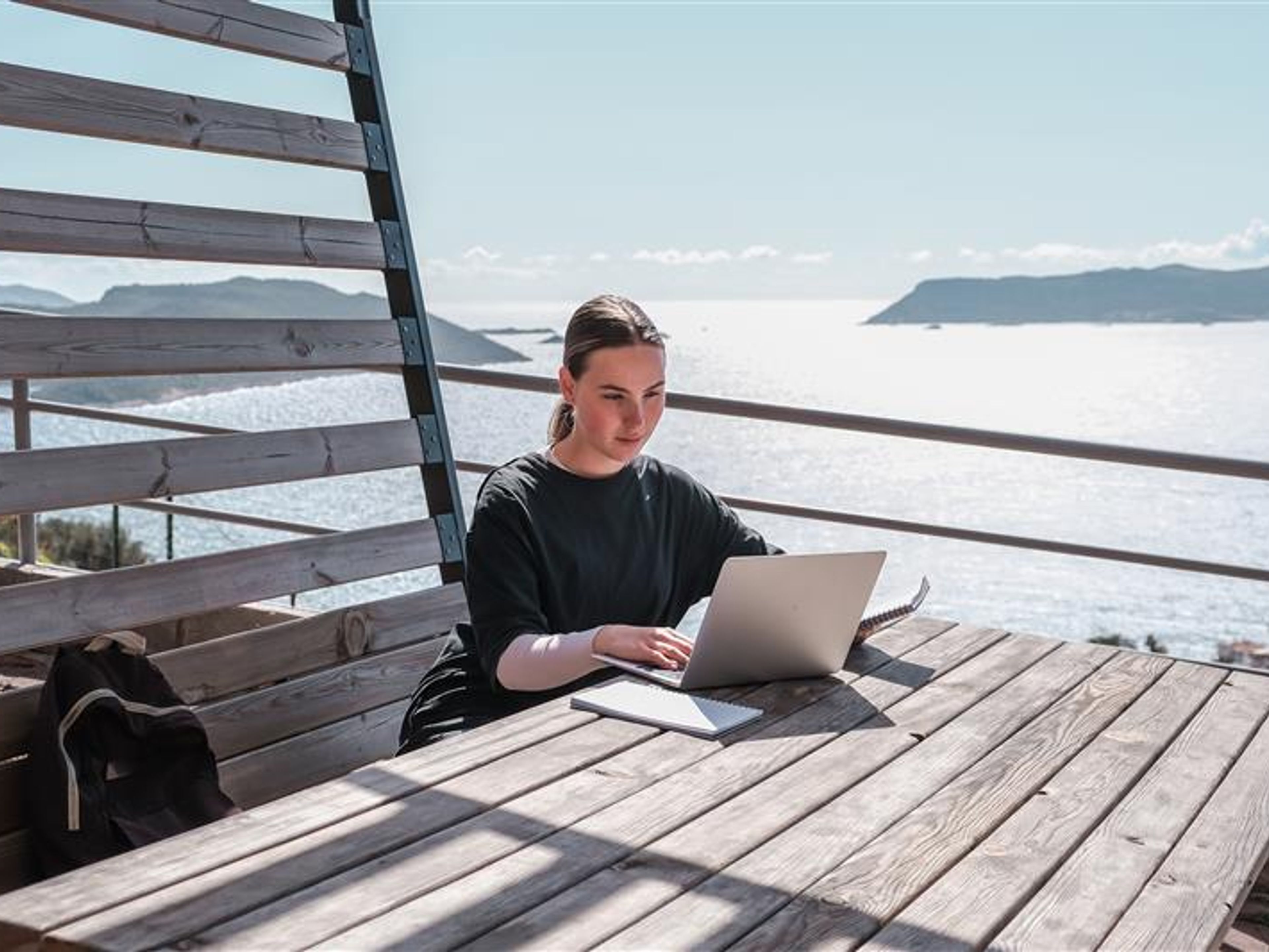 A woman working with a beach view behind 